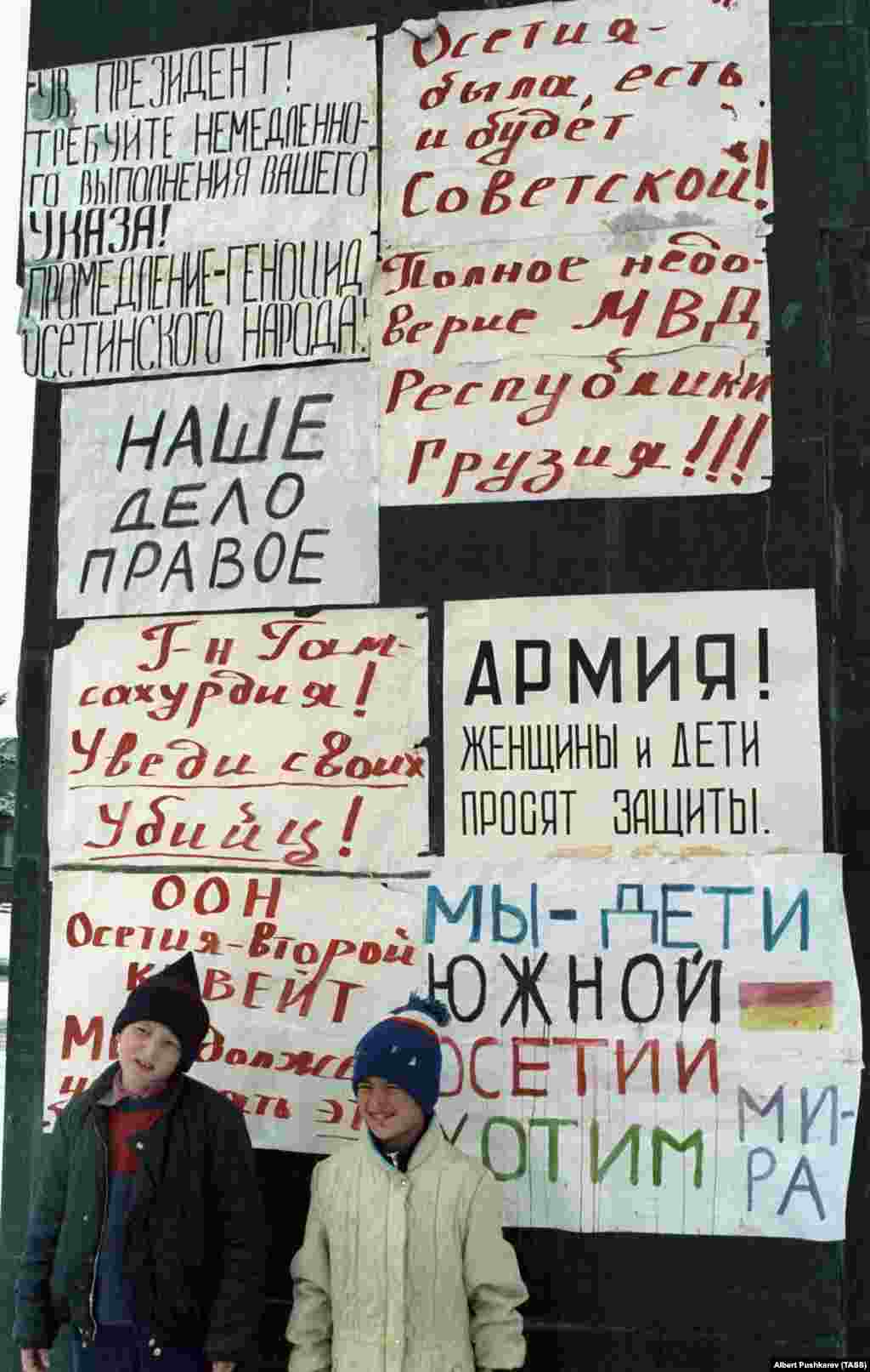 &quot;Осетия советтік болған, бола береді де!&quot; деген жазуы бар плакаттың астында тұрған балалар. 1 қаңтар 1991 жыл. Грузия Совет Одағынан бөлініп, тәуелсіз ел болуға талпынғанда көптеген грузин осетиндерден сескеніп, оларды &quot;бесінші колонна&quot; көрді. Ал осетиндер өздерін оқшауланғандай сезінді. Жаңа қабылданған заңдар грузин тілін мемлекеттік тіл етіп бекітіп, осетиндердің Тбилисидегі саяси өкілдігіне шектеу қойды.