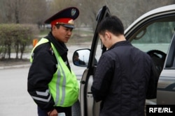 Автокөлік жүргізушісінің құжатын тексеріп тұрған полиция қызметкері.