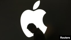 Apple компаниясының логотипі алдында тұрған адам. (Көрнекі сурет).